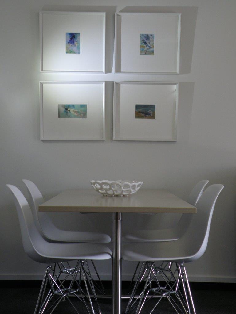 A dining table with four chairs and four pictures frames on the wall