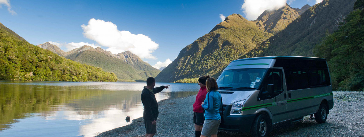 Three people standing on a Lake front next to a rental van